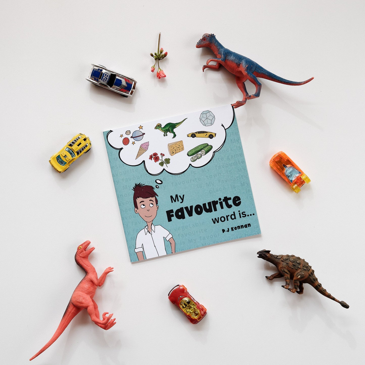Image of book on white background surrounded by objects such as dinosaurs, cars and flowers