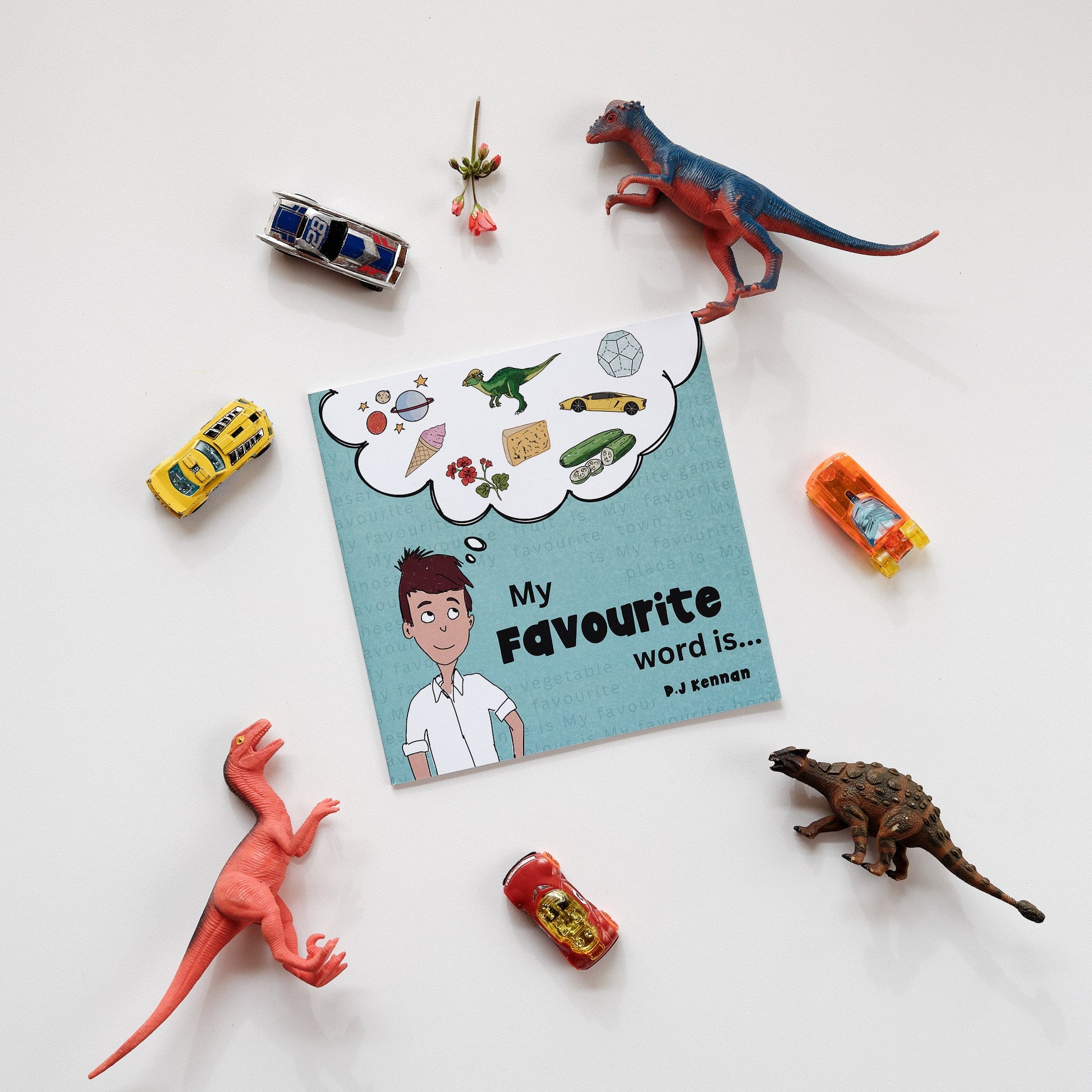 Image of book on white background surrounded by objects such as dinosaurs, cars and flowers